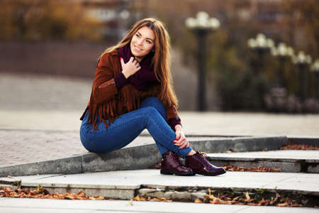 Happy young fashion woman in leather jacket sitting on city streetの写真素材