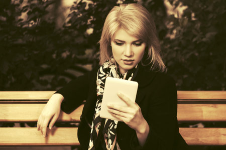 Young fashion blond woman with tablet computer sitting on bench