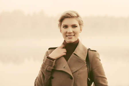 Young fashion woman in beige coat walking in a fog outdoorの写真素材