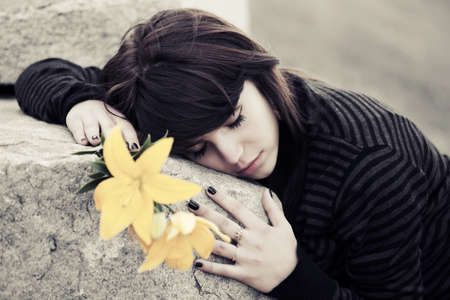 Sad young woman with a flowers lying on tombstoneの写真素材