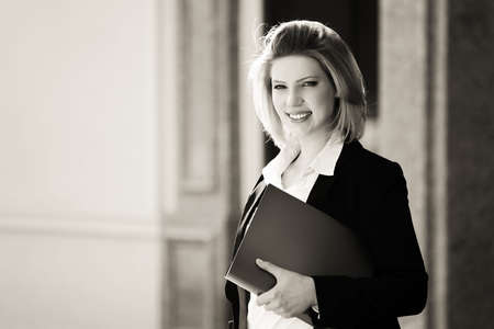 Happy young business woman with a folder standing at office buildingの写真素材