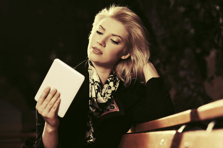 Young fashion blond woman with tablet computer sitting on bench