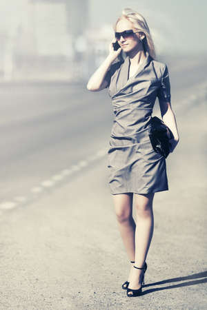 Young fashion blond woman calling on cell phone on city streetの写真素材
