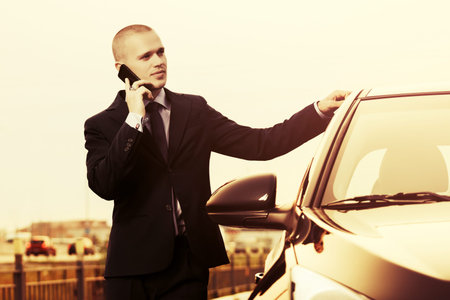 Young handsome businessman calling on cell phone next to his car