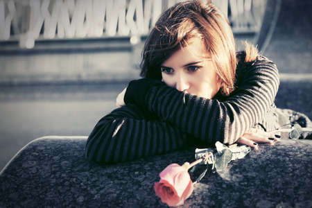 Sad young woman with a red rose on city streetの写真素材