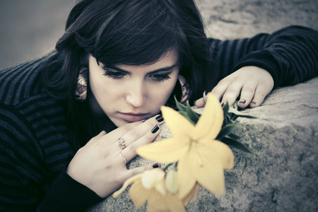 Sad young woman with a flowers lying on tombstone
