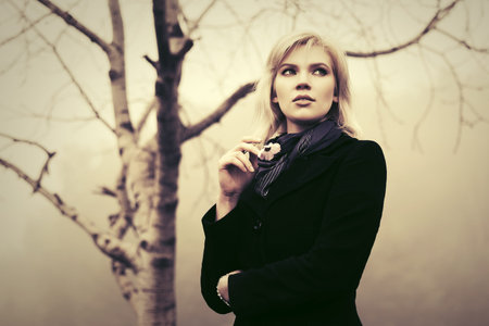 Young fashion woman in black coat walking in a fog outdoor