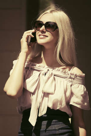 Happy fashion blond woman in sunglasses calling on mobile phoneの写真素材