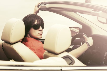 Young man in sunglasses driving convertible carの写真素材