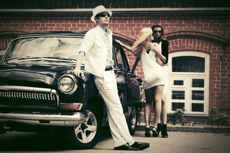Happy young fashion man and women next to vintage car