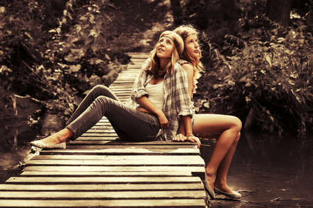 Two happy teen girls sitting on wooden bridge in summer forestの写真素材