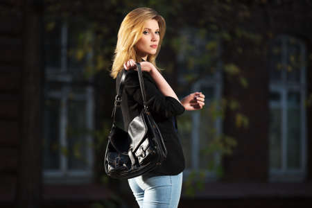 Young fashion blond business woman with handbag walking in night on city streetの写真素材