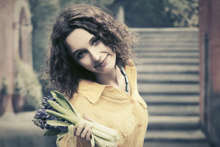 Happy young fashion woman with bouquet of flowers walking in city streetの写真素材