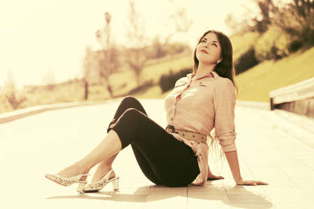 Happy young fashion woman sitting on the sidewalk in city parkの写真素材