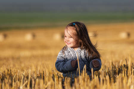 Happy 2 year old girl walking in a summer harvested fieldの写真素材