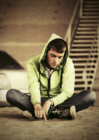 Sad young fashion man sitting on the ground outdoor