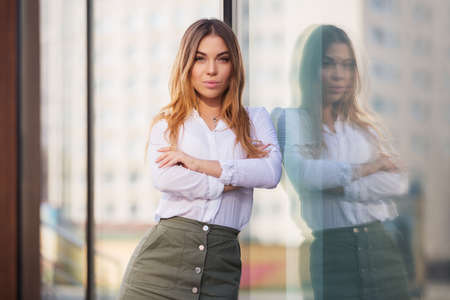 Young fashion woman standing next to mall window in a city street. Stylish female model in white blouse and short skirt outdoorの写真素材