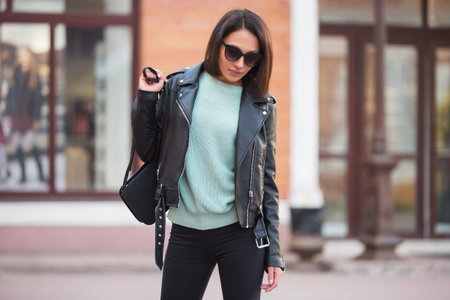 Young fashion woman with handbag walking in city street Stylish female model in black leather jacket outdoorの写真素材