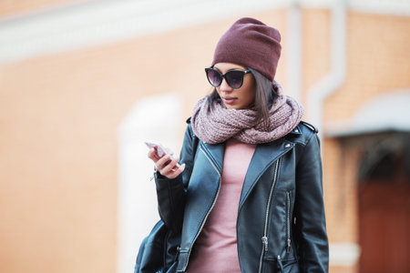 Young fashion woman in black leather jacket using cell phone in city street. Stylish female model...