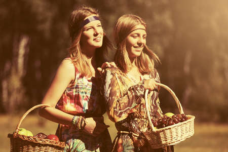 Happy teen girls with a fruit basket walking on nature. Stylish fashion model outdoorの写真素材
