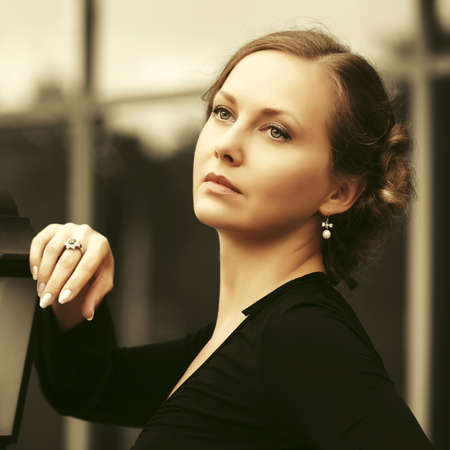 Sad beautiful fashion woman in black blouse with bun updo hairstyle walking in city streetの写真素材