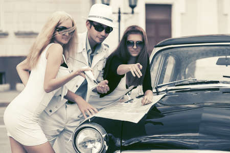 Young fashion people with a road map next to vintage car の写真素材