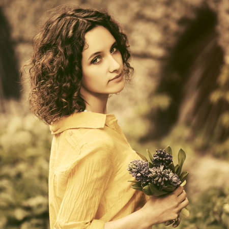 Happy young fashion woman in yellow shirt with bouquet of flowers walking in city streetの写真素材