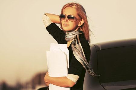 Fashion business woman with financial papers next to her car Stylish female model wearing black...