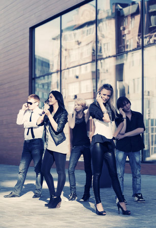 Young fashion people calling on cell phones on city street Stylish trendy men and women outdoor