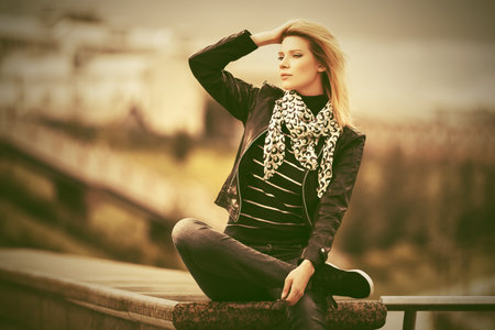 Happy young fashion blond woman wearing black leather jacket and white scarf outdoor