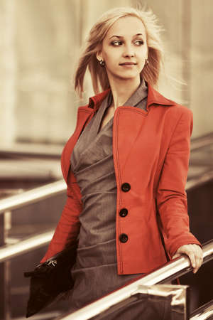 Young fashion blond business woman with handbag wearing orange jacket walking on city streetの写真素材