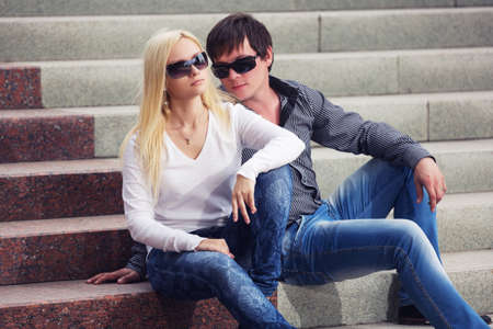 Happy young fashion couple on the steps Stylish trendy man and woman in  sunglasses and blue jeansの写真素材