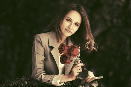 Happy young woman with red roses leaning on railing Stylish fashion model in light grey blazer...