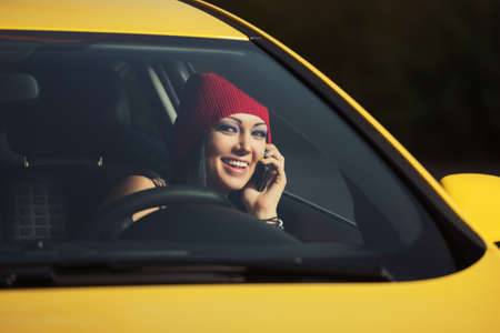 Young fashion woman in red beanie calling on cell phone driving a carの写真素材