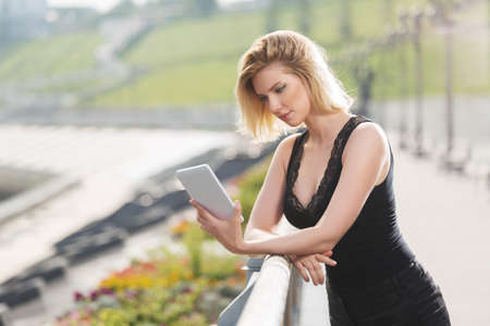 Young fashion woman using digital tablet computer on city street  Stylish female model with blonde hairs in black tank topの写真素材