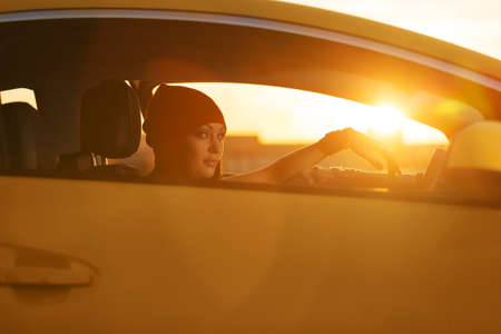 Young stylish fashion woman in red beanie driving a car の写真素材