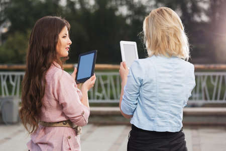 Two young fashion women using digital tablet computers on city streetの写真素材