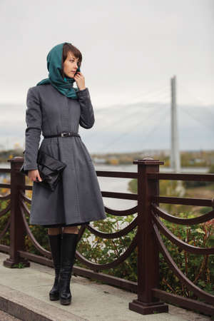 Young fashion woman with handbag walking on city street Stylish female model in gray classic coat and head scarf の写真素材