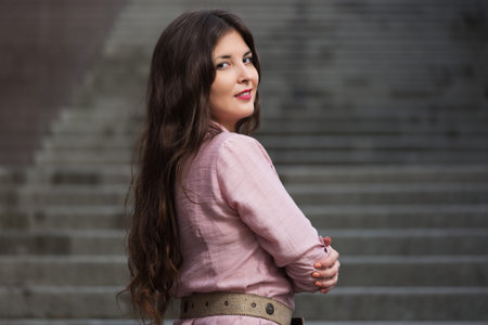 Happy young fashion woman walking on city street Stylish female model with long brown hairs in light...