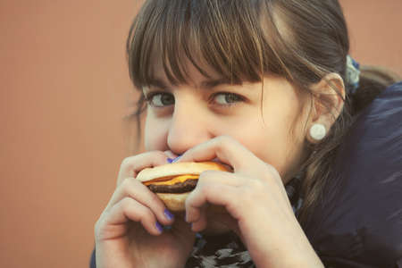 Happy teen girl eating a burger on city streetの写真素材