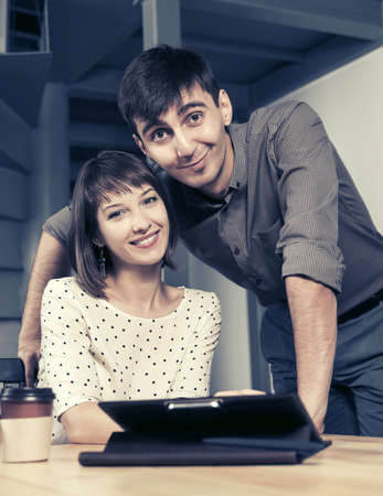 Happy young business couple using digital tablet computer sitting at the tableの写真素材