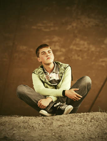 Sad teen boy in depression sitting on the ground Stylish trendy male model in light green hoodie and dark blue jeansの写真素材