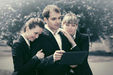 Young business people using laptop in city park Stylish man and women in black suit jacketsの写真素材