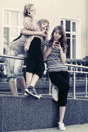 Group of happy teenage girls using cell phones against a school buildingの写真素材