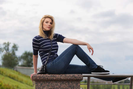 Young fashion woman sitting on parapet  Stylish female model in striped turtleneck t-shirt and dark blue jeansの写真素材