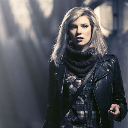 Young fashion blonde woman walking on city street at night Stylish female model in black leather jacketの写真素材