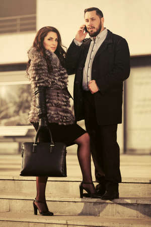 Happy young fashion couple walking on city street Stylish trendy man in classic black coat and woman in fox fur jacketの写真素材