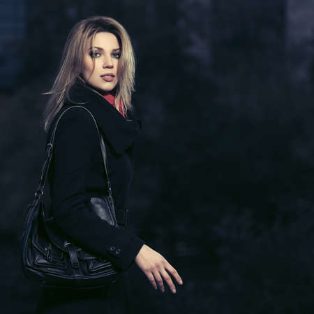 Young fashion blonde business woman walking on city street Stylish female model in classic black coat with leather handbagの写真素材