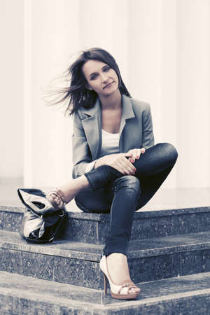 Happy young fashion woman sitting on steps Stylish female model in gray blazer and dark blue jeansの写真素材