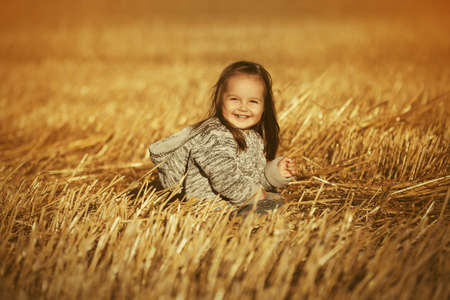 Happy two year old girl in knitted hoodie sweatshirt walking in summer harvested fieldの写真素材